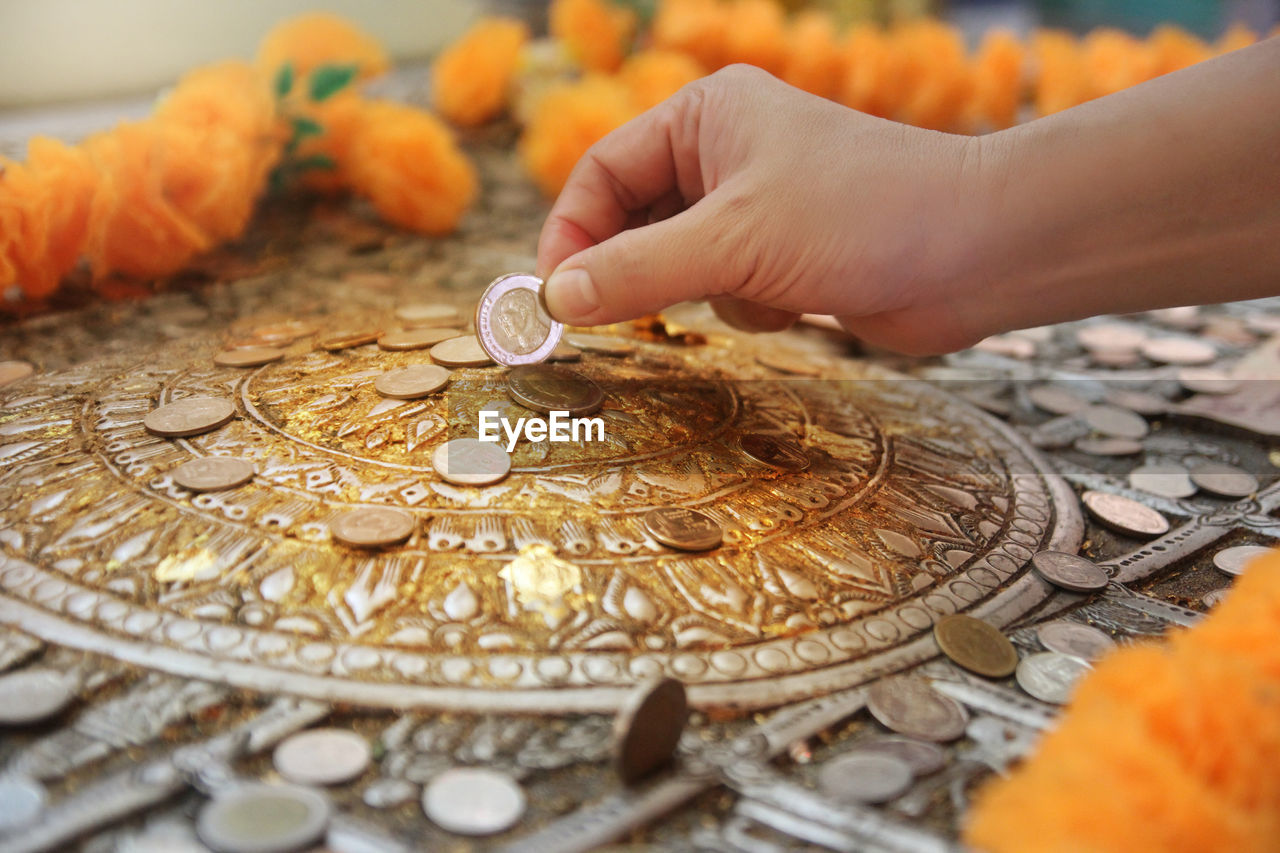 Close-up of hand putting coin into religious coin bank