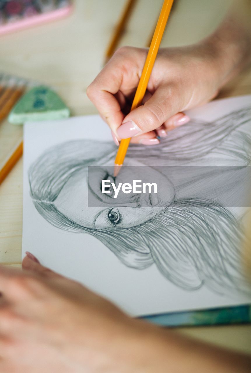 Cropped hands of woman sketching female on paper at table