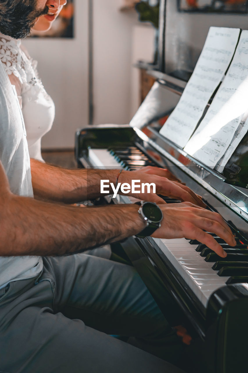 Midsection of man playing piano by woman with notes