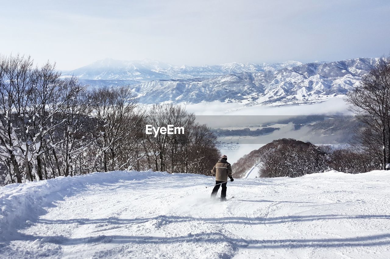 Rear view of man skiing on snow covered mountain against sky