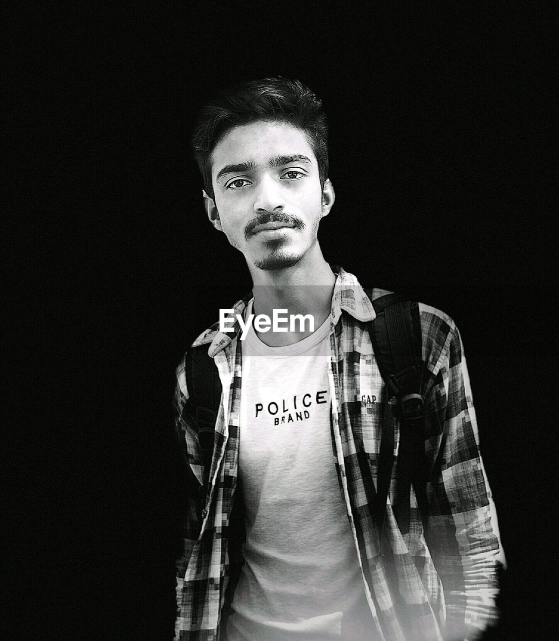 Portrait of young man standing against black background