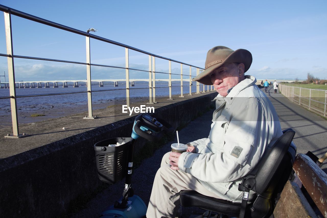 Man sitting on motorised scooter by sea against sky