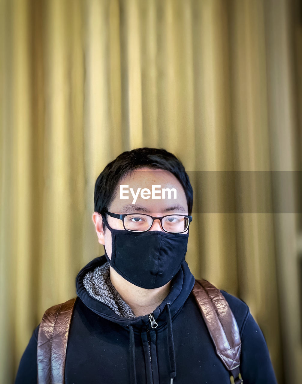 Portrait of young man wearing eyeglasses and face mask against wall.