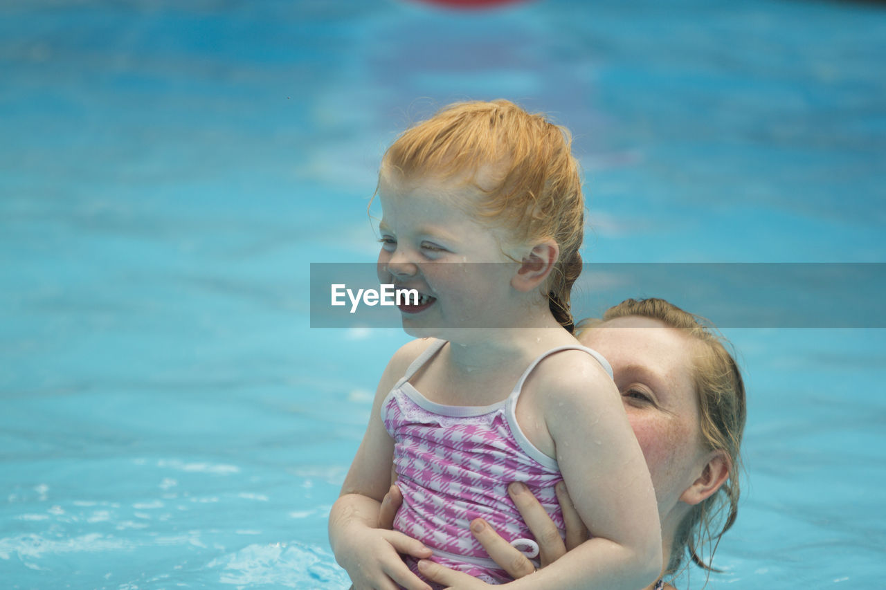 Mother holding smiling girl in swimming pool
