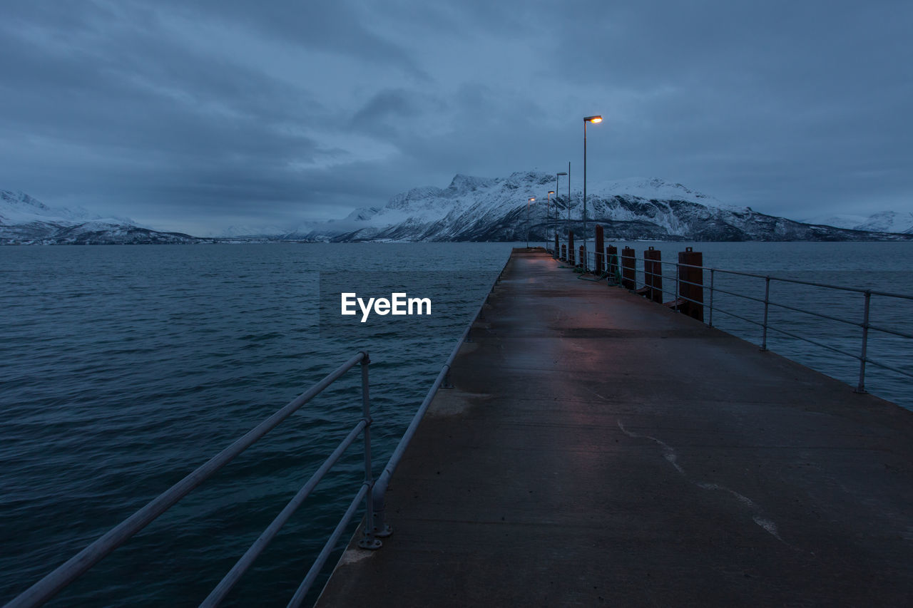 Wet pier over sea against sky at dusk