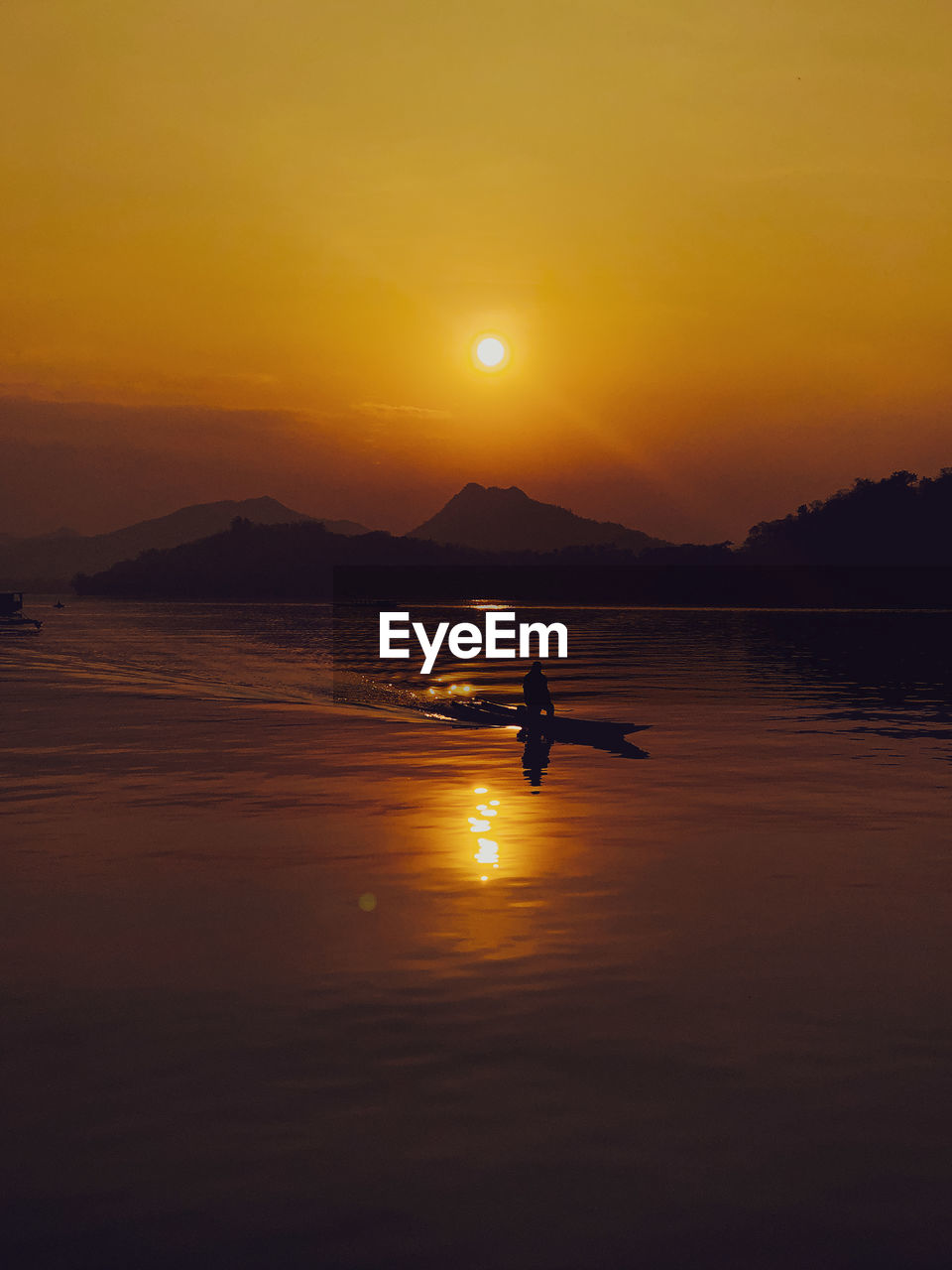 Silhouette man on sea against orange sky during sunset