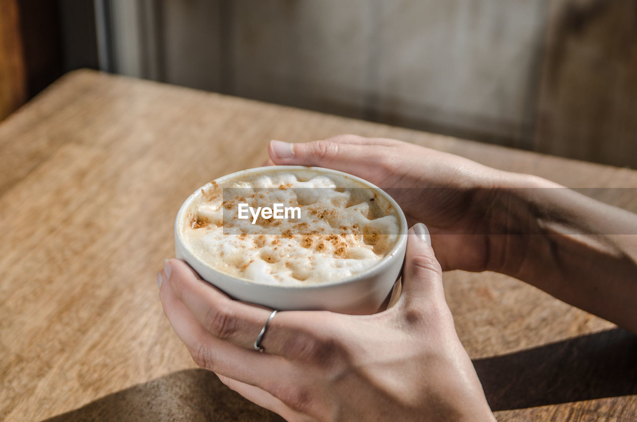 Cropped image of hands holding latte macchiato on table