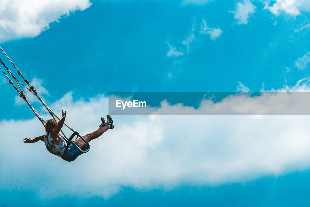 Low angle view of woman swinging against cloudy sky