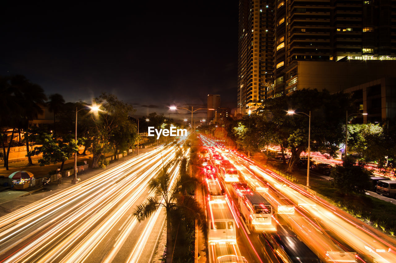 Light trails on city street amidst buildings at night