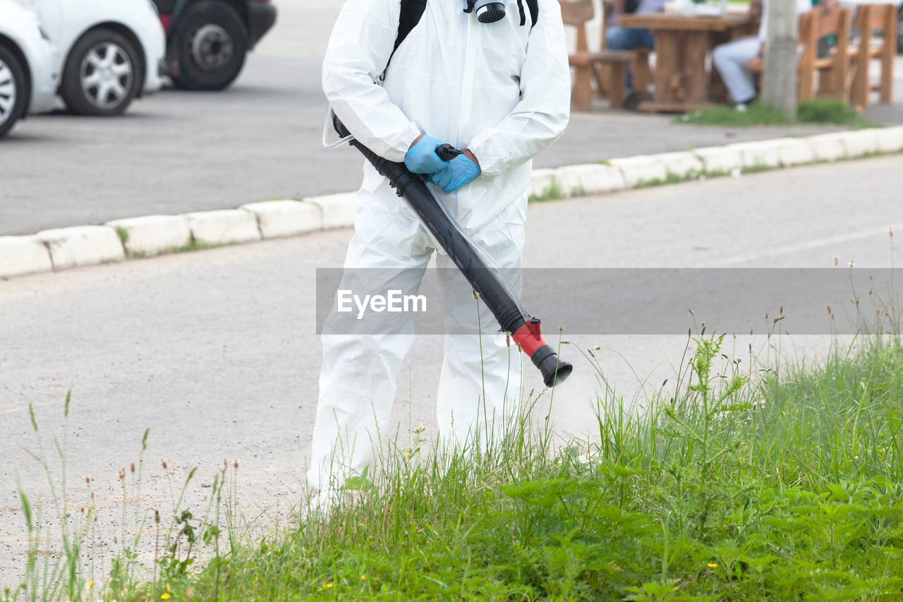 Midsection of worker spraying chemicals on plant