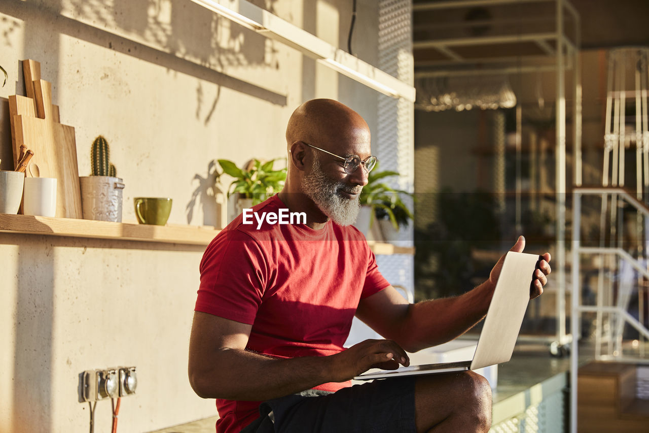 Smiling businessman concentrating on work while using laptop at home