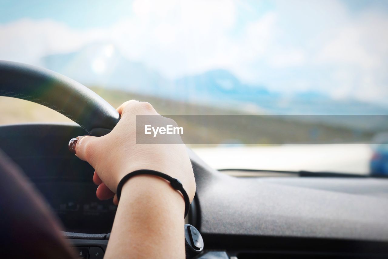 Cropped hand of woman holding steering wheel in car