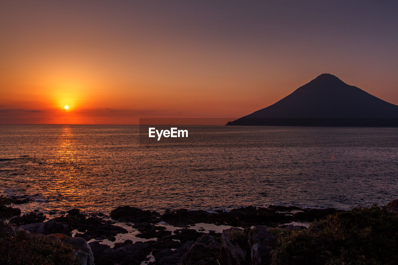 Scenic view of sea and silhouette mountain against sky during sunset