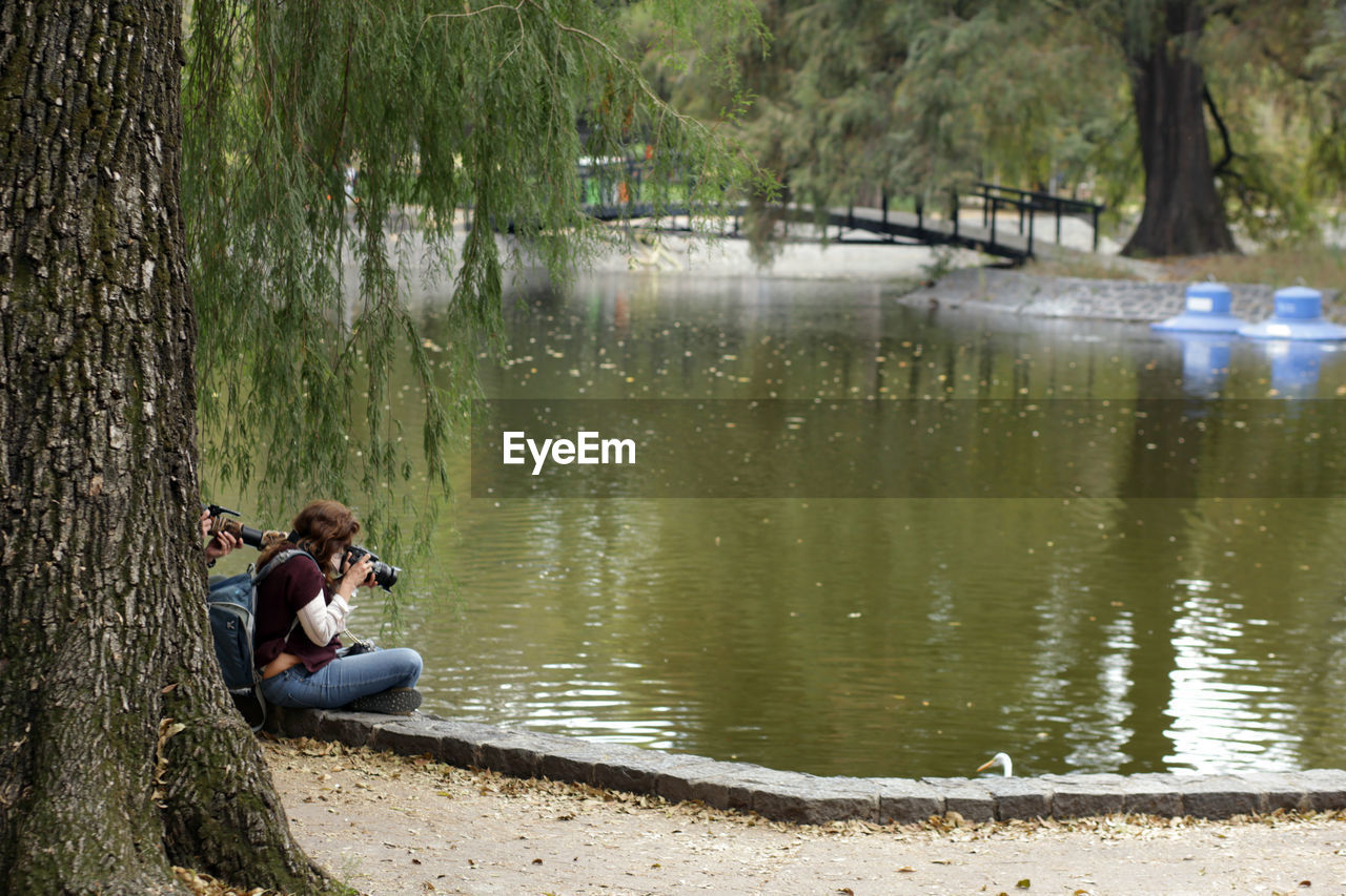 SIDE VIEW OF MAN SITTING ON LAKE