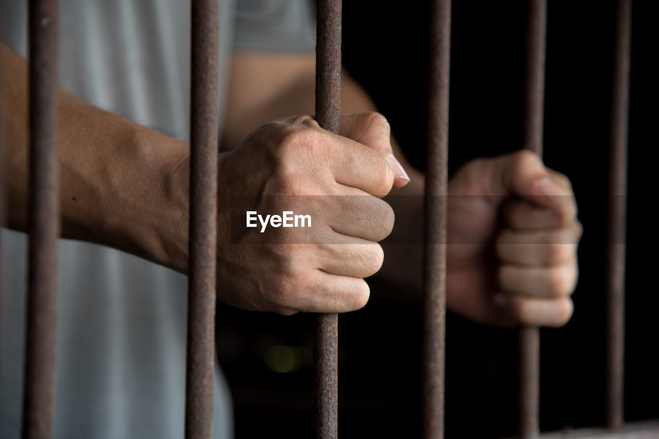 Close-up of man holding prison bars