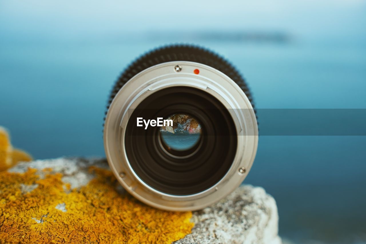 Close-up of camera lens against sea on rock