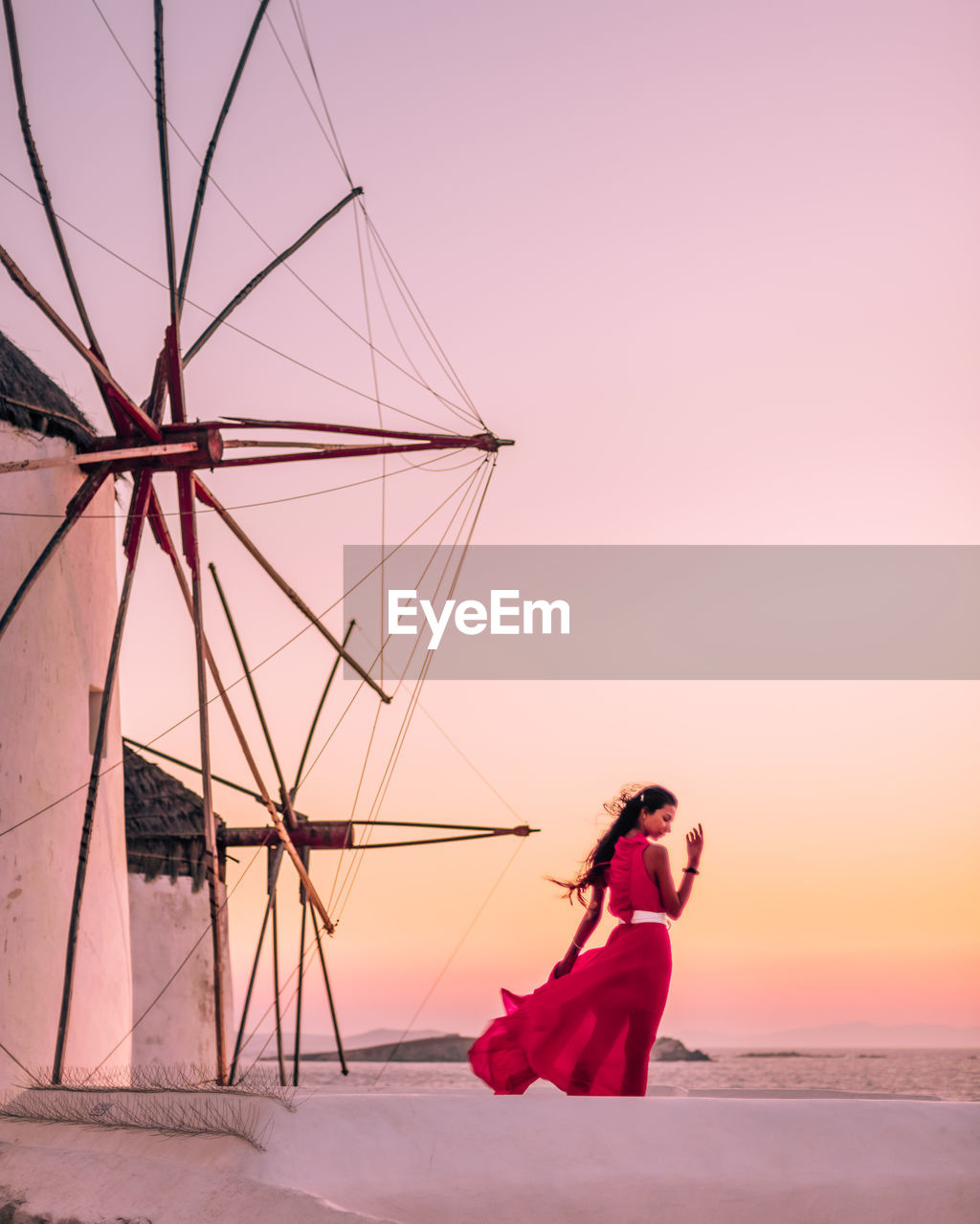 Rear view of woman standing by windmill against sky during sunset