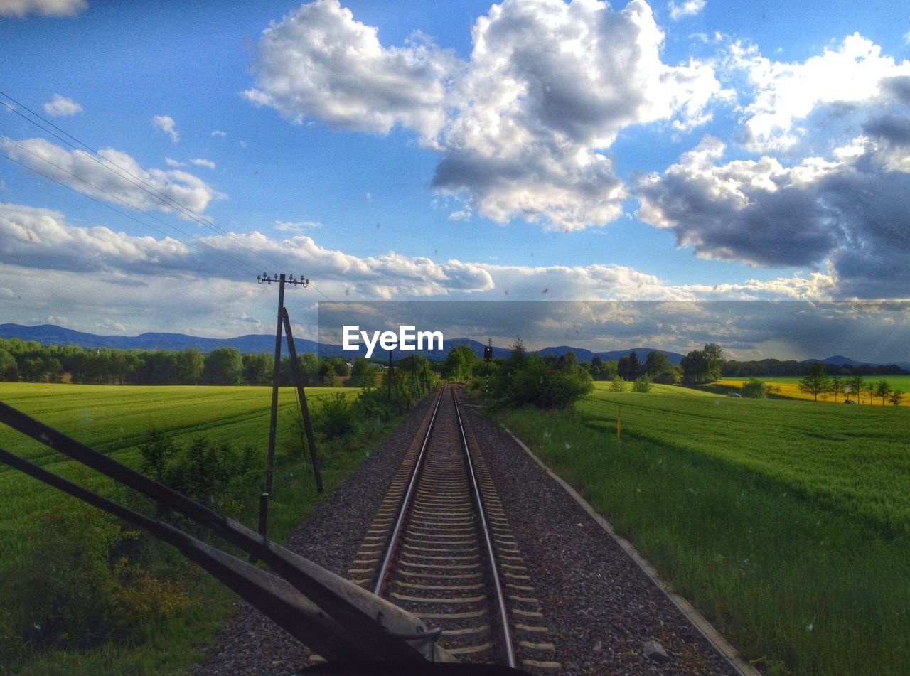 Railroad tracks on grassy field seen through train windshield