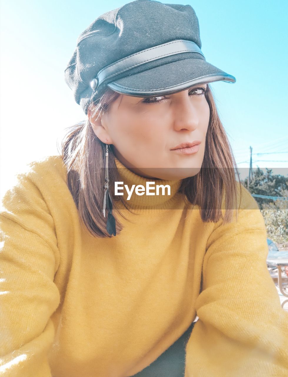 Portrait of beautiful young woman in cap against sky