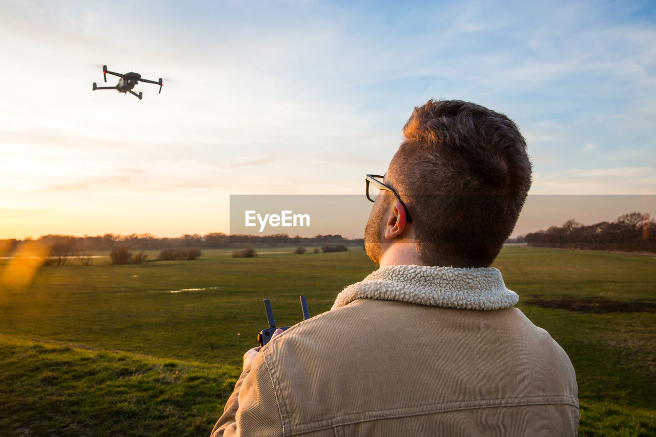 Man flying drone over field against sky during sunset