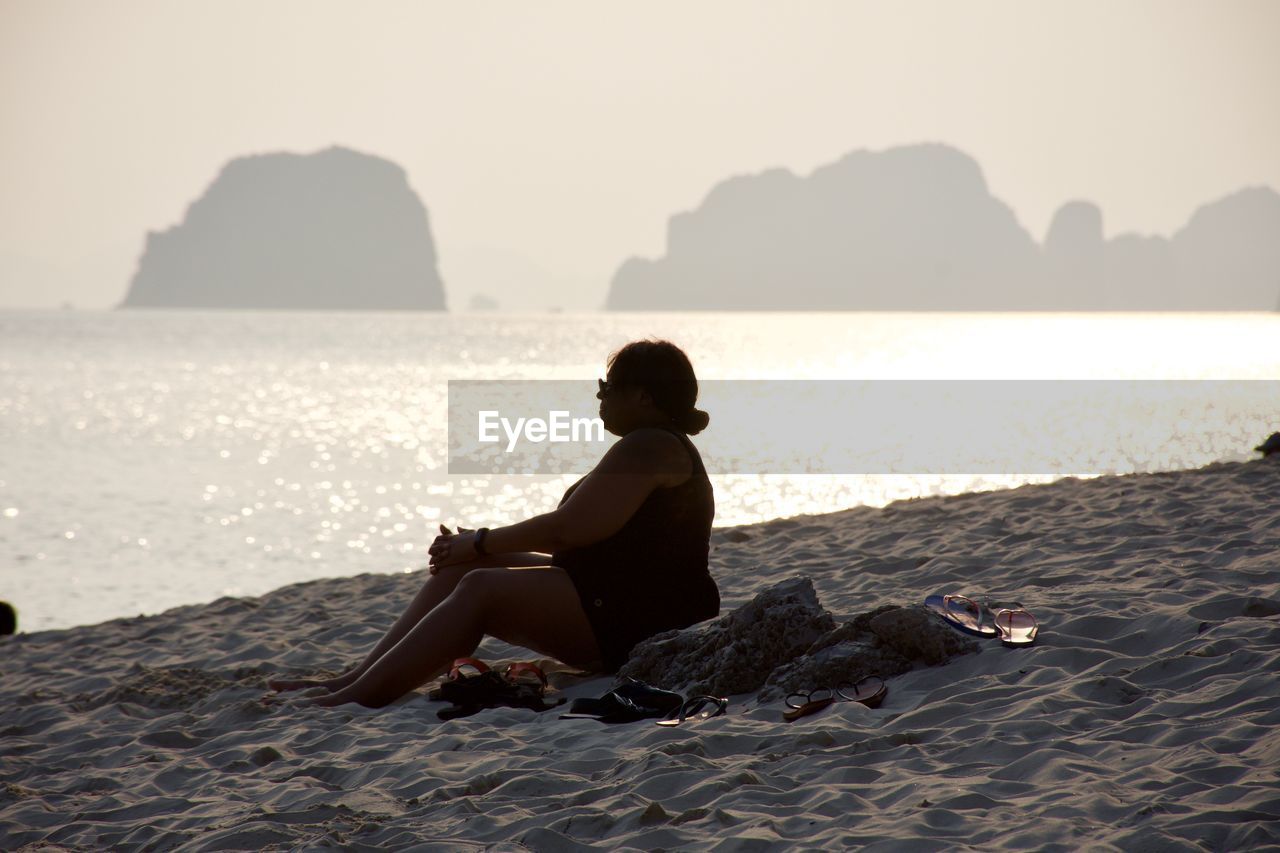 Woman sitting shore at beach against sky