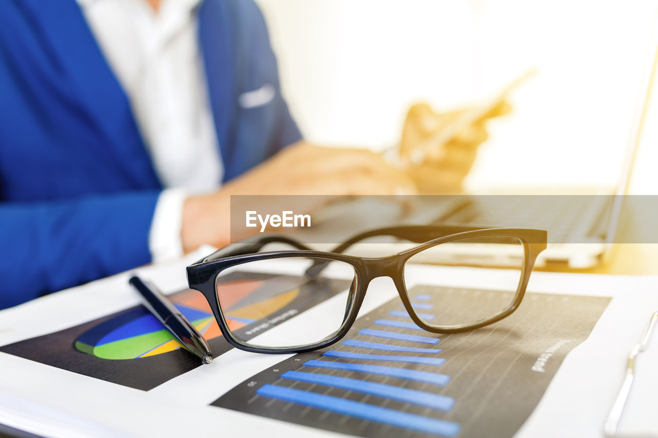 Midsection of businessman using phone with eyeglasses at desk