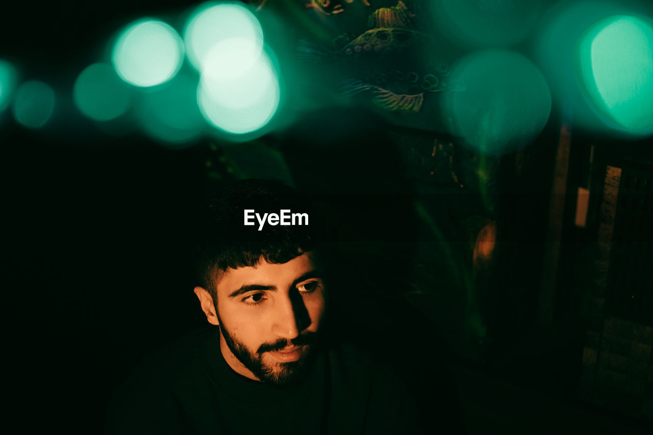 Young beard man looking away under illuminated green lights at restaurant