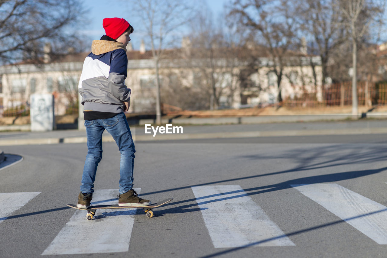 Rear view of boy skateboarding on road