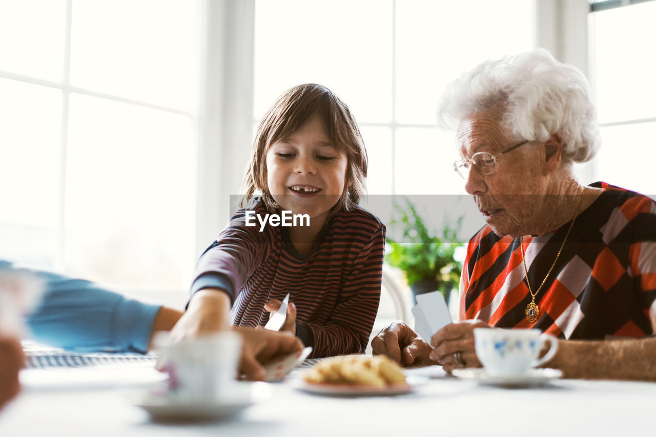 Happy boy playing cards with great grandmother and mother at table