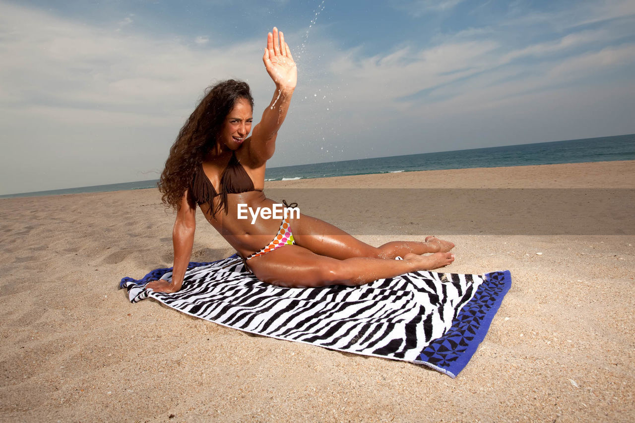 YOUNG WOMAN LYING ON SAND AT BEACH