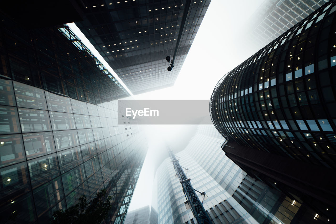 Low angle view of modern buildings against sky during foggy weather