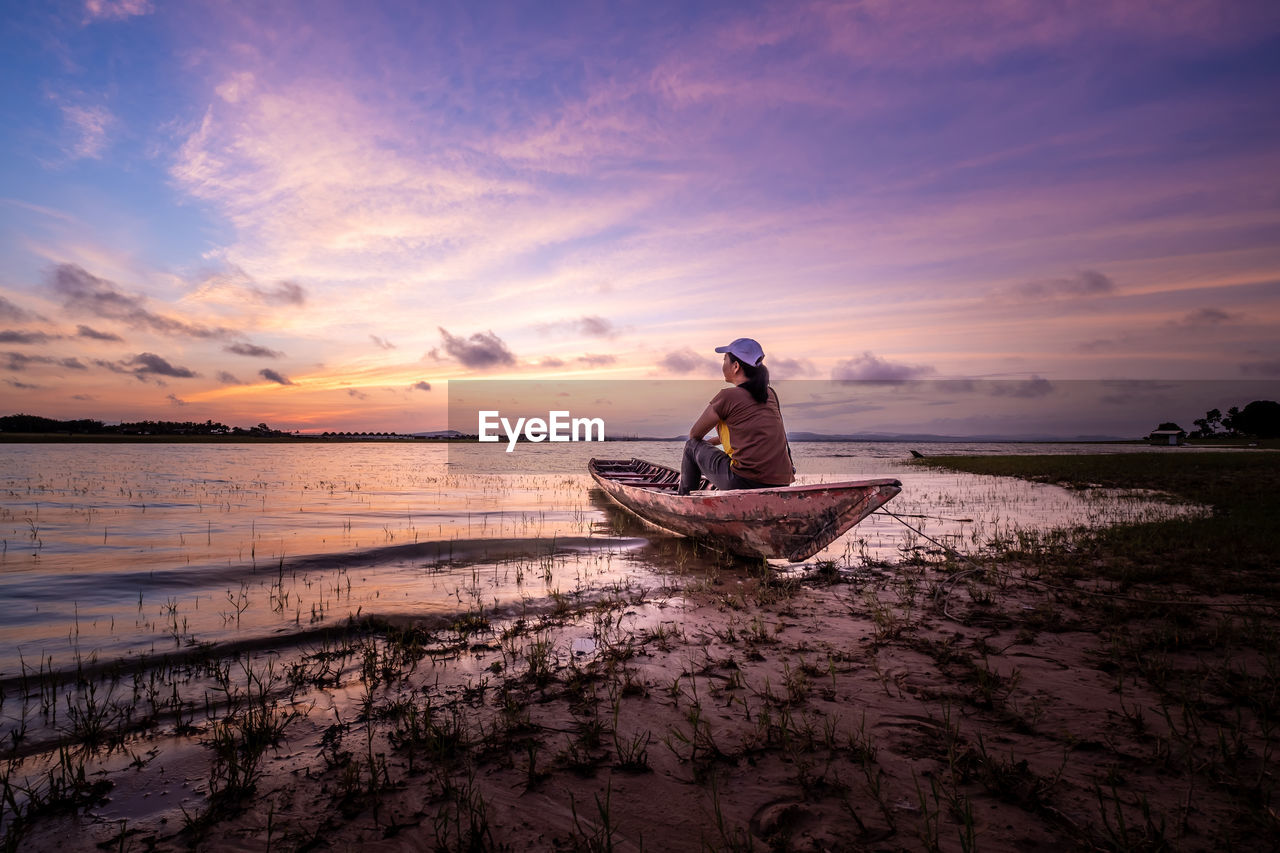 Man on boat at beach against sky during sunset