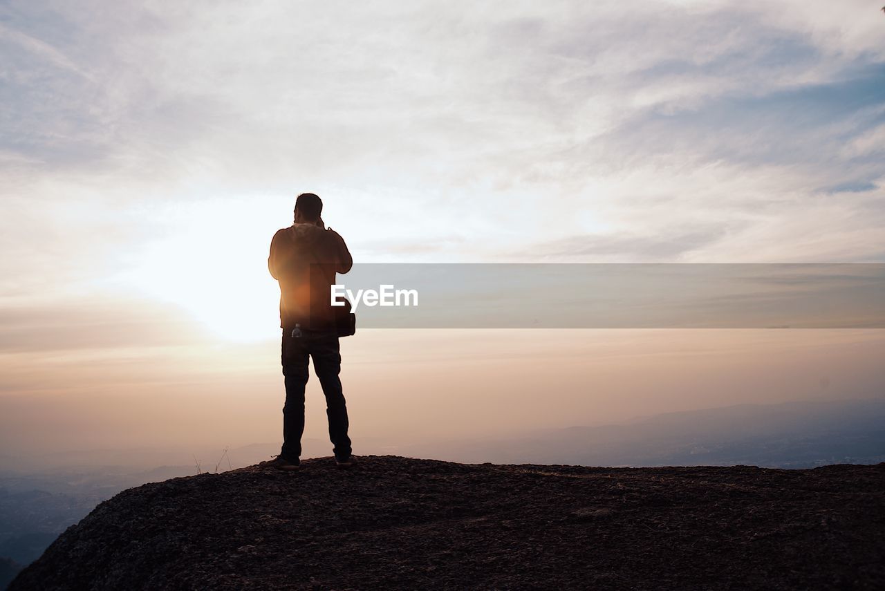 Rear view of silhouette man standing on mountain during sunset