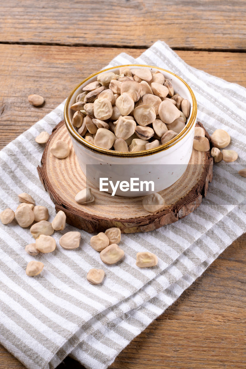 Dry raw cicerchia or indian pea on a ceramic bowl with napkin on wooden background, close up