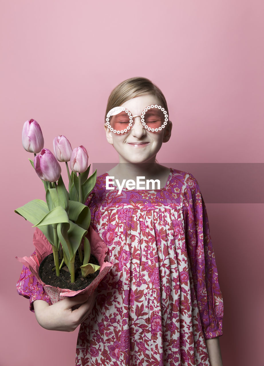 Mod, quirky girl, fair skin, holding pink tulips on pink backdrop