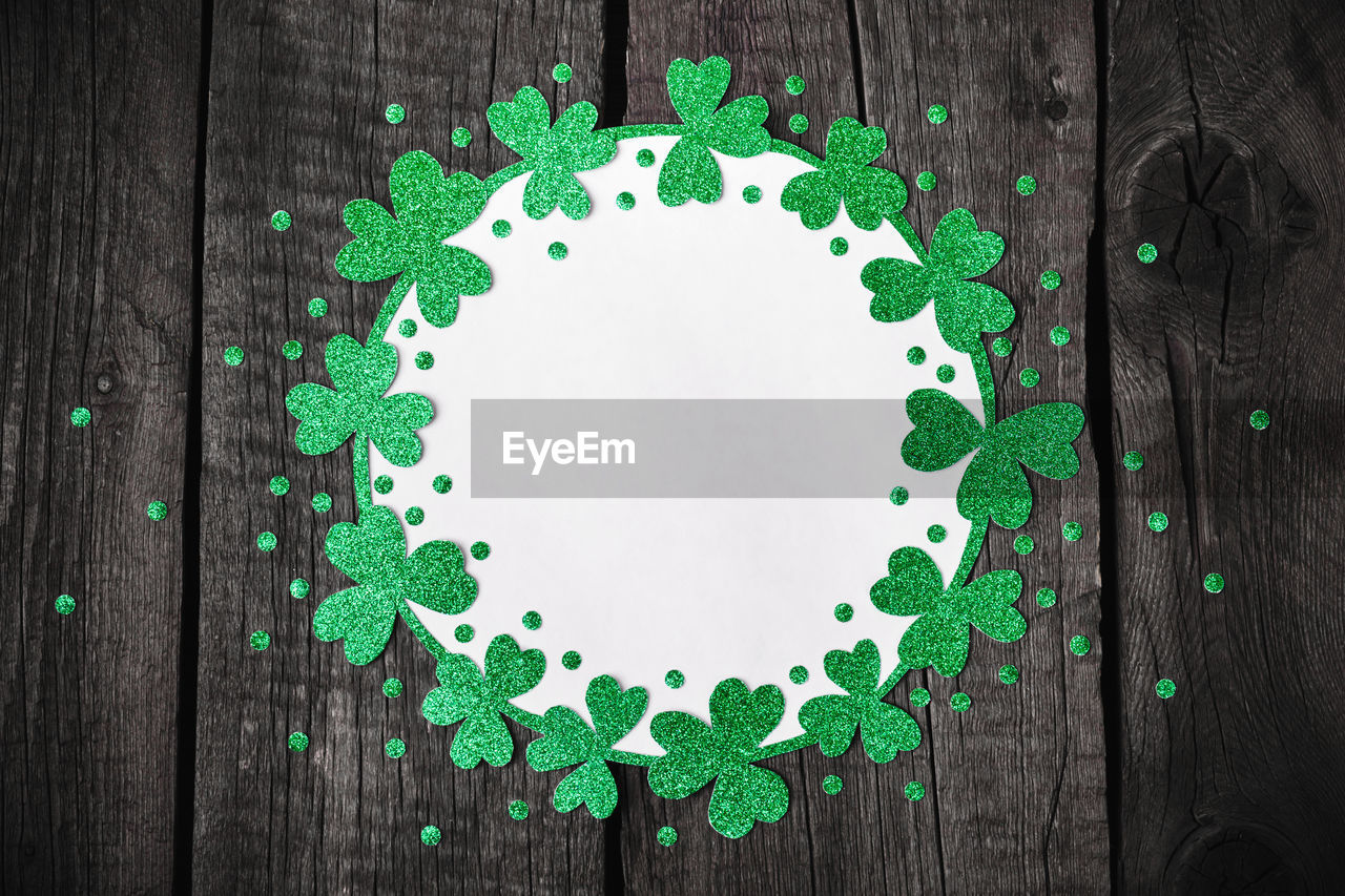 St. patricks day background. round frame of shiny shamrocks and confetti on rough wooden background.