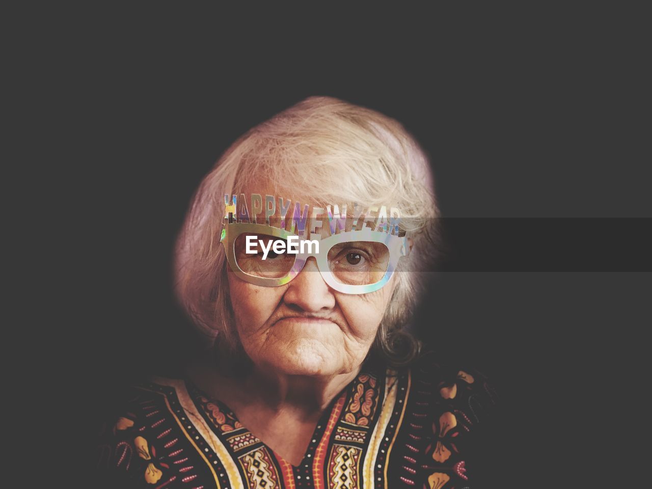 Portrait of senior woman wearing novelty glasses against black background