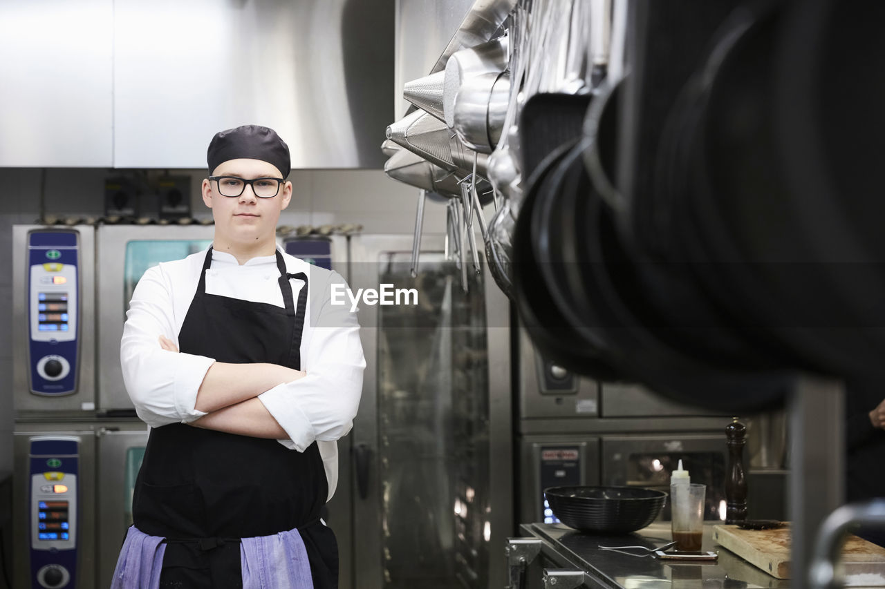 Portrait of male chef student standing arms crossed in commercial kitchen