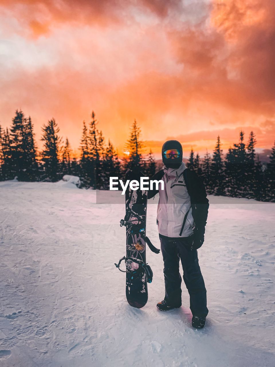 Rear view of man standing on snow covered field against sky during sunset