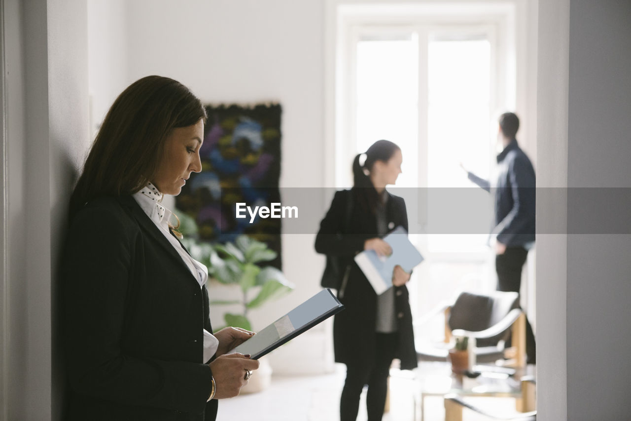 Side view of female realtor reading brochure with couple in background