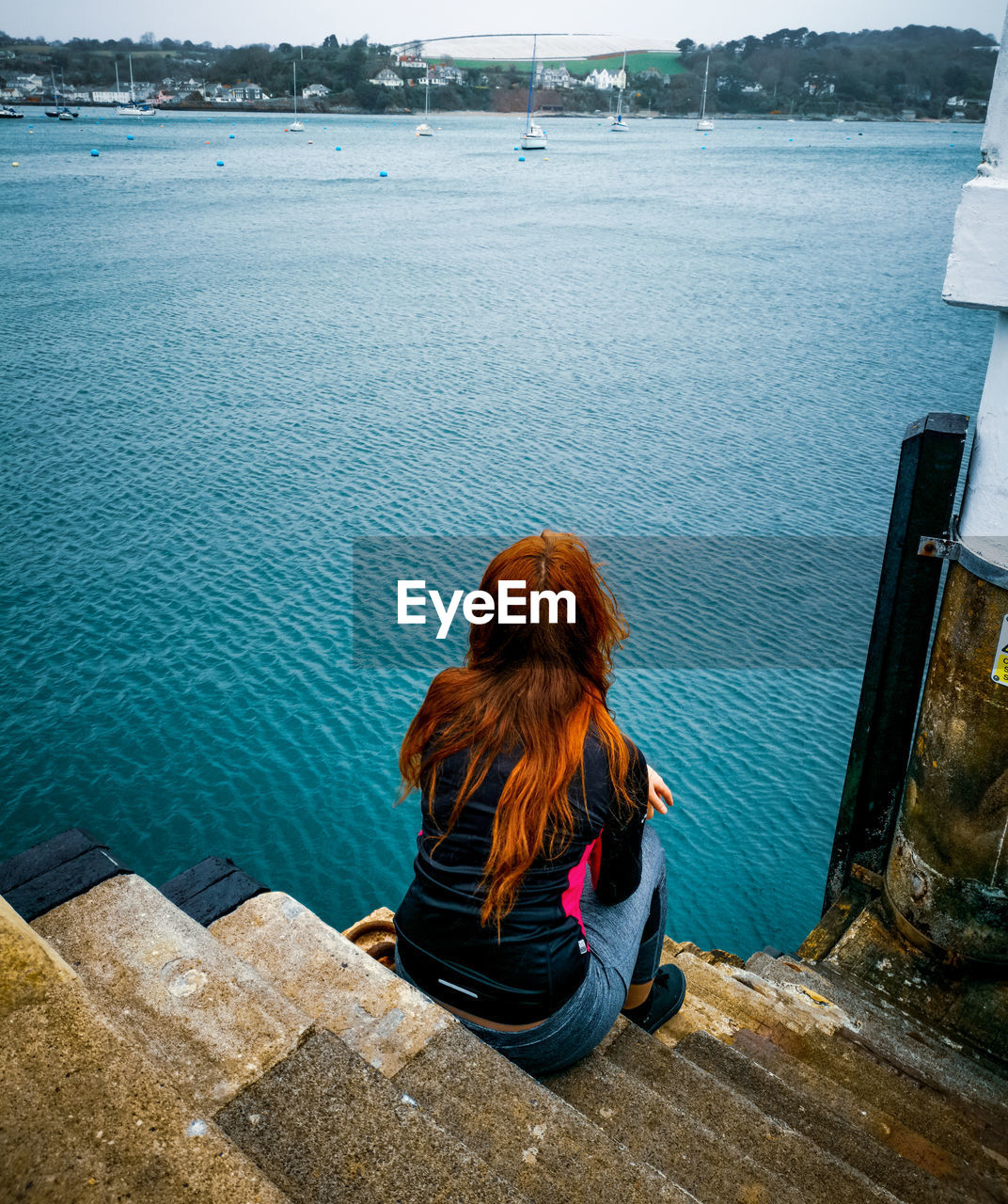 Rear view of woman looking at sea while sitting on staircase