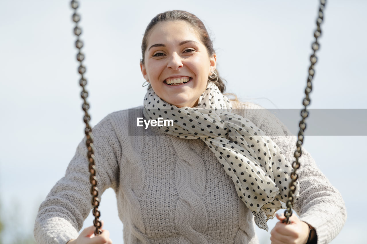 Portrait of smiling young woman swinging against clear sky