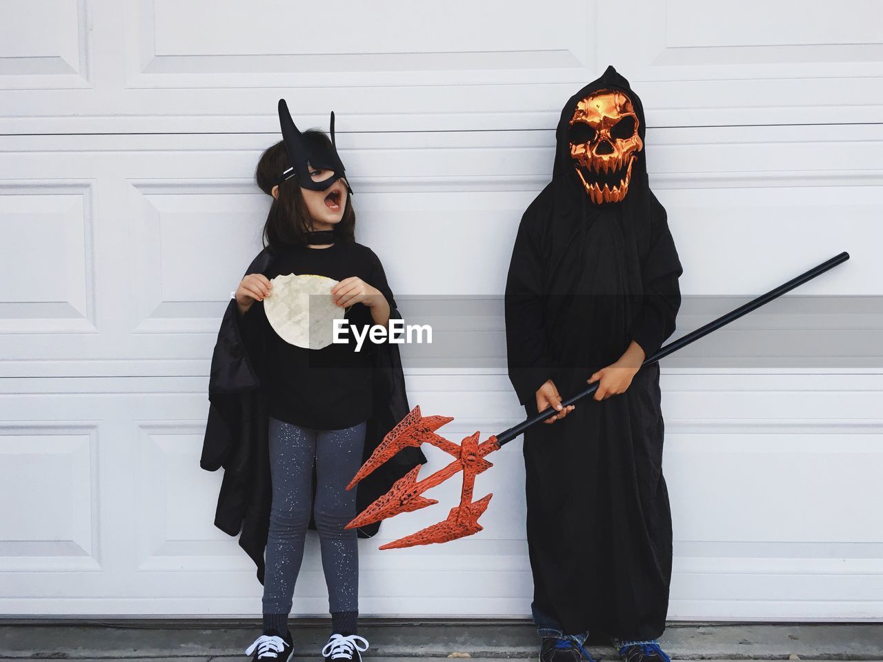 Girl and boy in halloween costume standing against wall