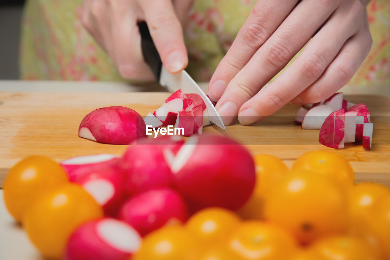 The fingers of a young woman cooking in the kitchen cut radishes and tomatoes, close-up