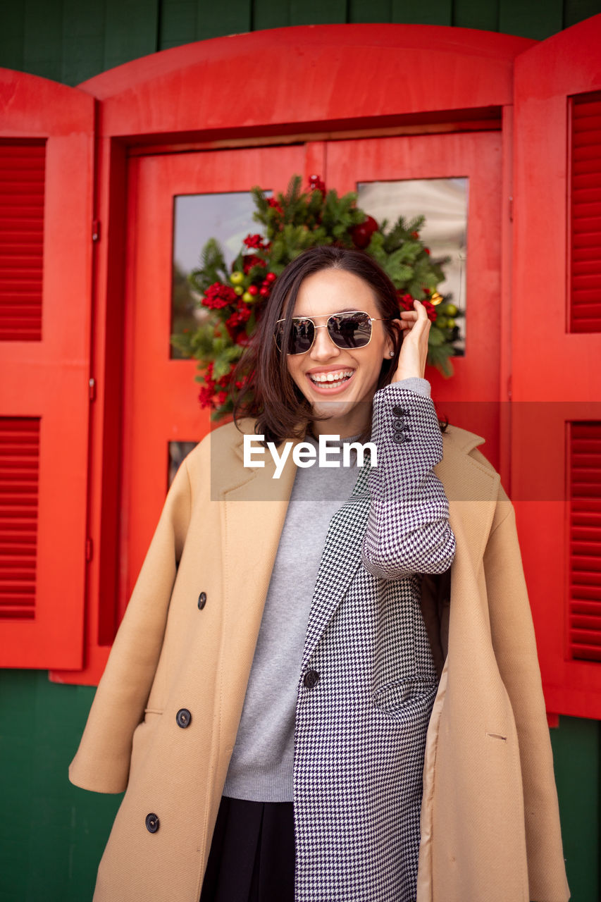 portrait of young woman wearing sunglasses standing against wall