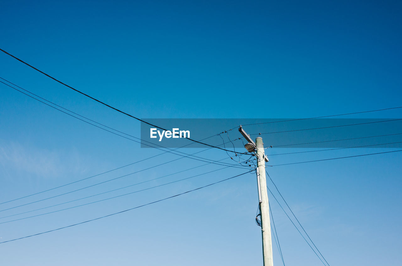 Low angle view of electricity pylon against blue sky