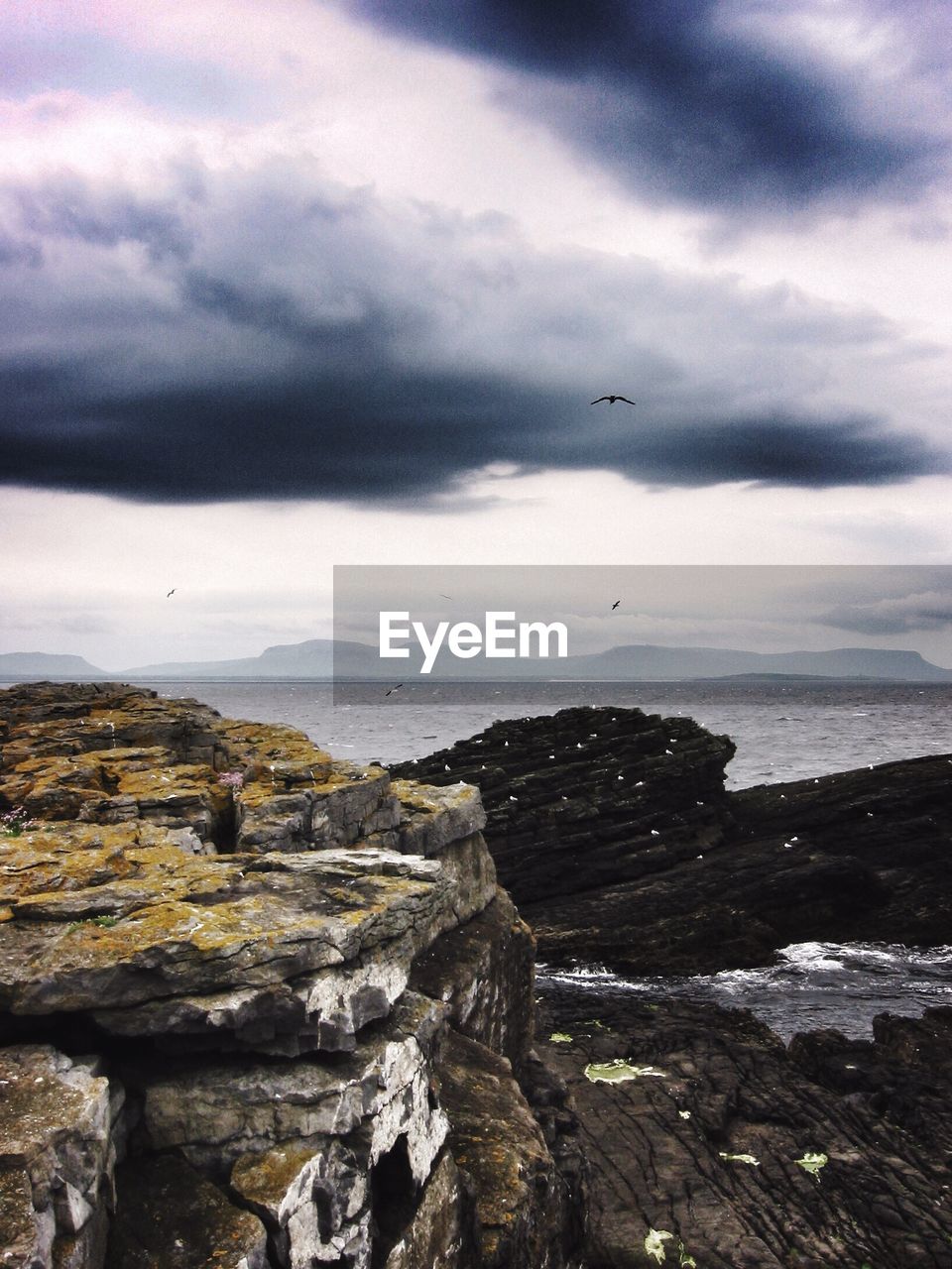 Rock formation by sea against cloudy sky