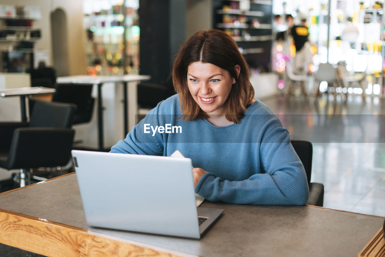 Beautiful stylish young woman plus size body positive using laptop at the beauty salon office