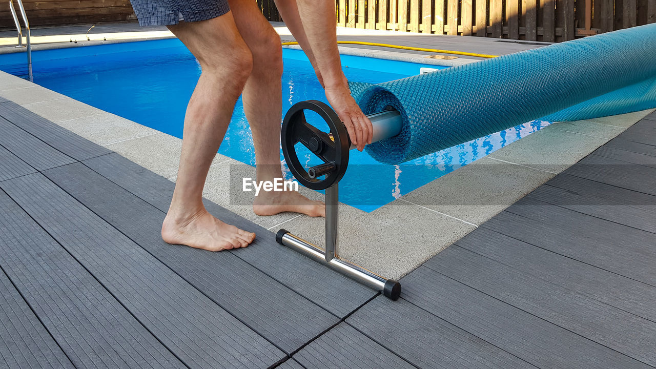 Low section of man standing on footpath by swimming pool