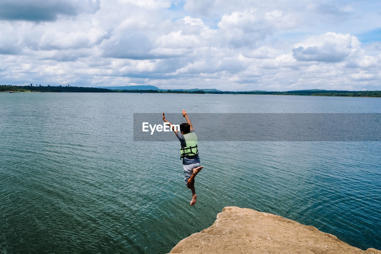 Rear view of man jumping in sea against sky